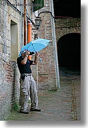 cobblestones, europe, italy, men, people, photographers, siena, tourists, towns, tuscany, umbrellas, vertical, photograph