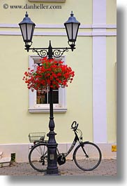 bicycles, bikes, europe, flowers, hungary, lamps, parked, posts, tarcal, under, vertical, photograph